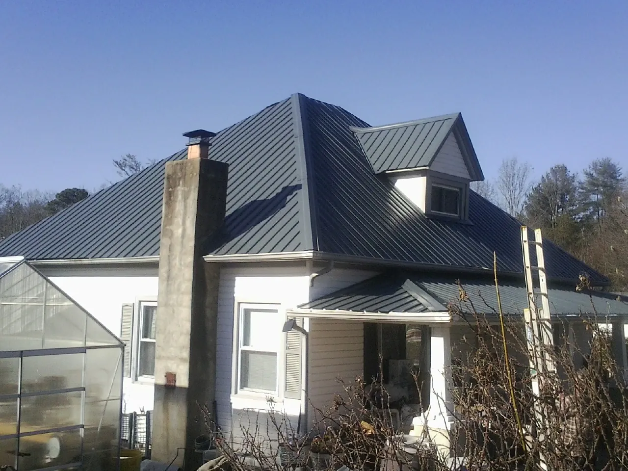Dark blue standing seam metal roof on a white farmhouse with dormer — Slate & Tile Roof Repair by Roofing Brothers in Coal Valley