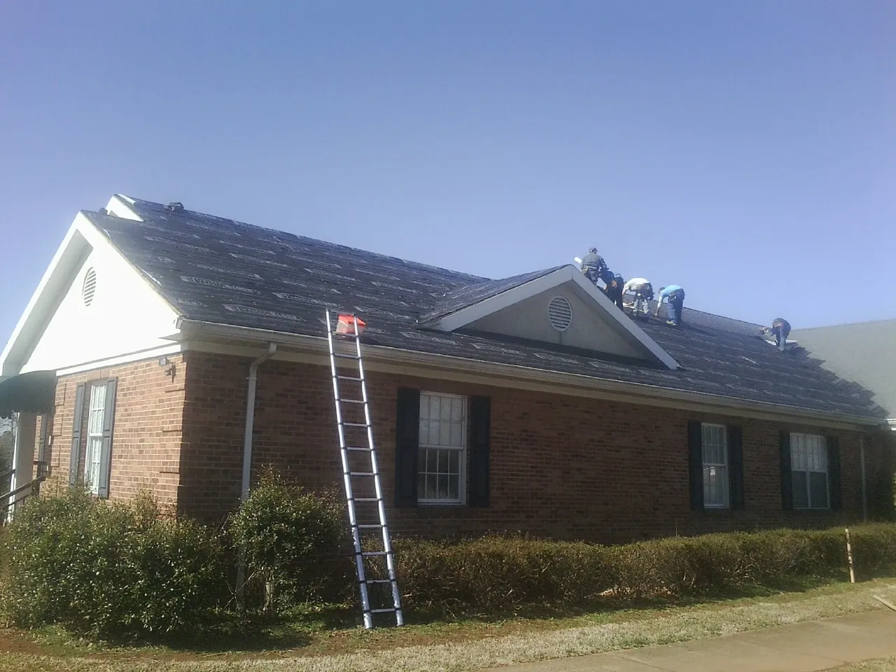 Crew tearing shingles off a brick ranch roof with a ladder set — Metal Roof Repair work by our crew in Coal Valley