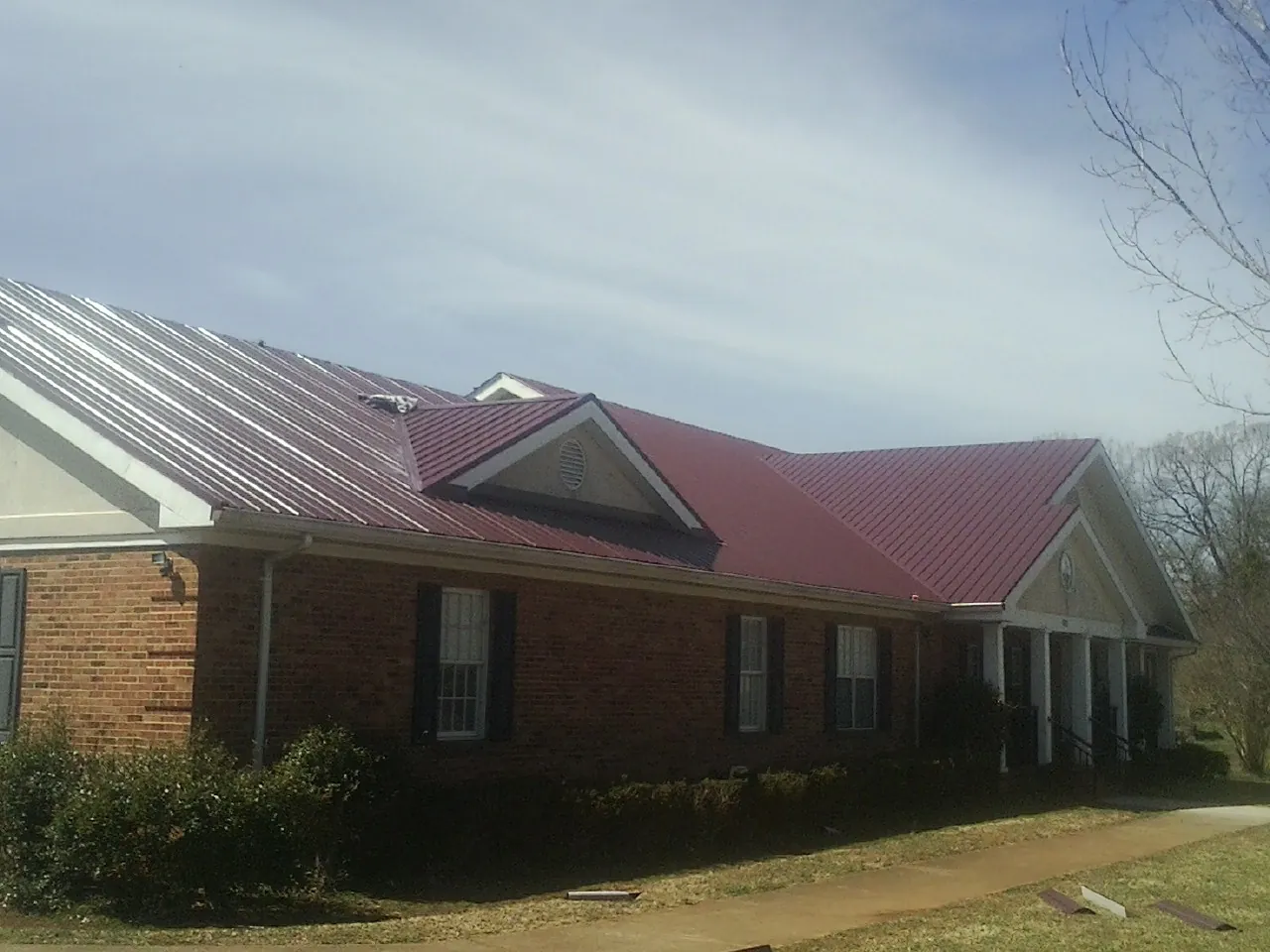 Red metal roof with gabled entries on a long brick building, from a Hail Damage Roof Repair job in Coal Valley