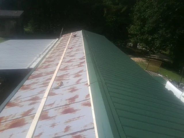 Old rusted panels beside newly installed green metal roofing — Wind Damage Roof Repair by Roofing Brothers in Coal Valley