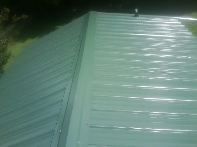 New green metal panels meeting at the ridge of a roof — Flat Roof Repair work by our crew in Coal Valley
