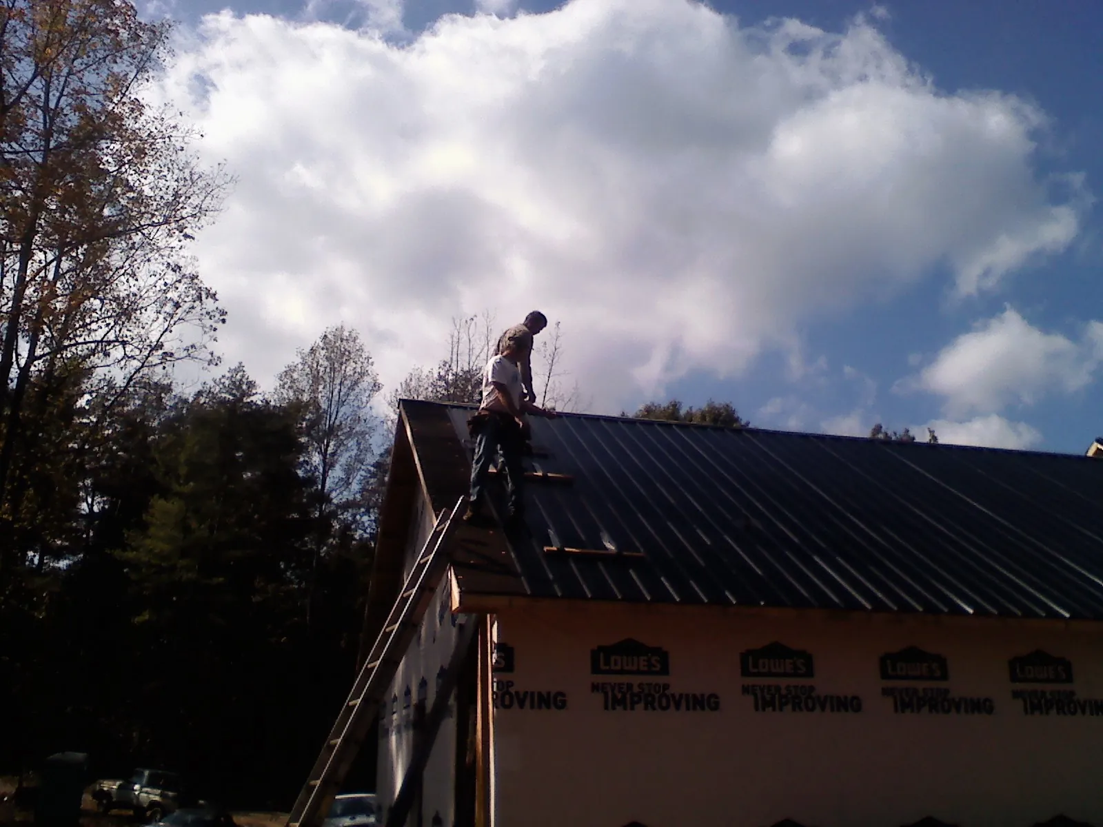 Roofer fastening dark metal panels high against a cloudy sky, from a Roof Inspection job in Coal Valley
