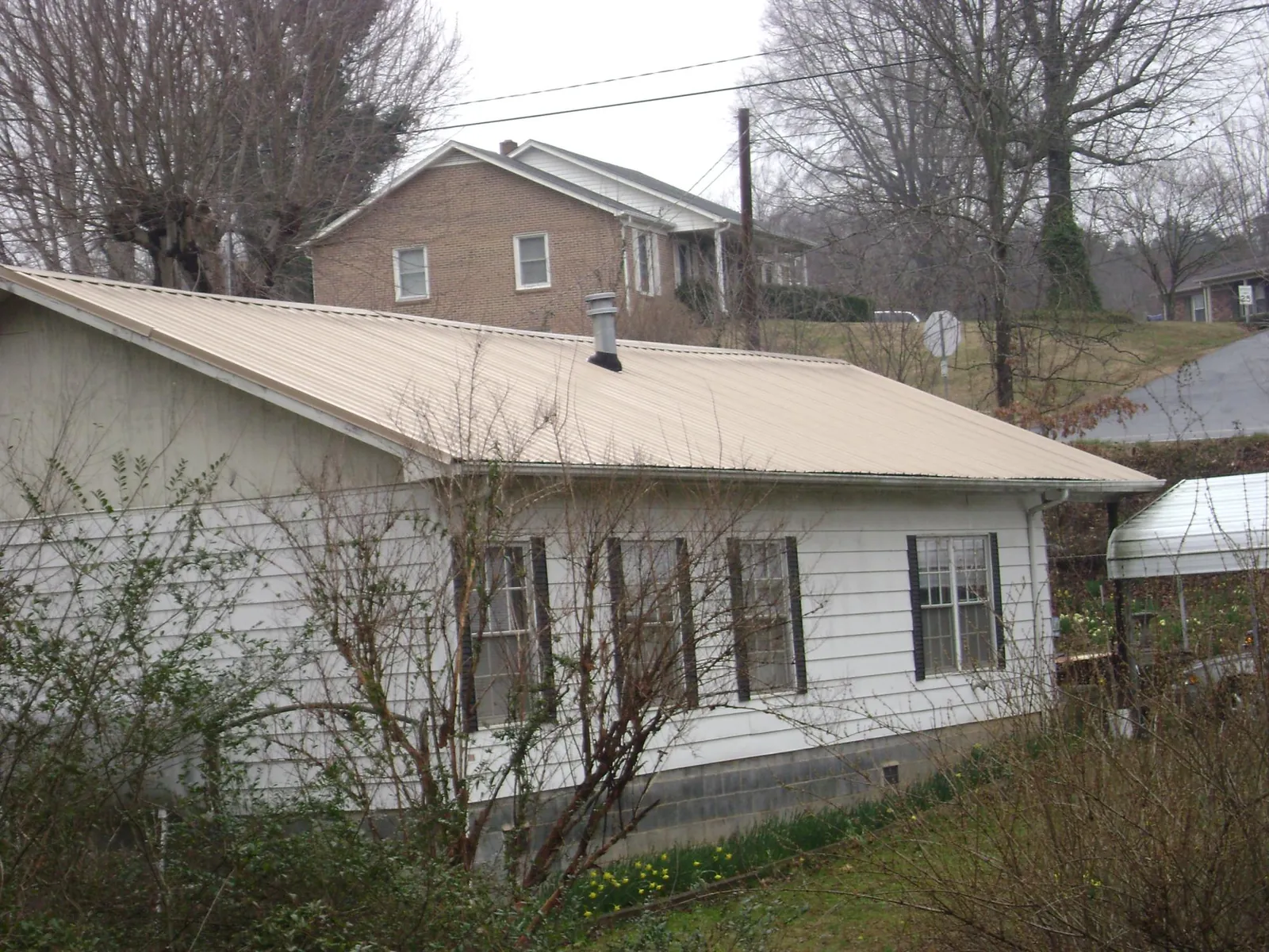 Tan metal roof on a white sided house set into a hillside — Commercial Roofing by Roofing Brothers in Coal Valley