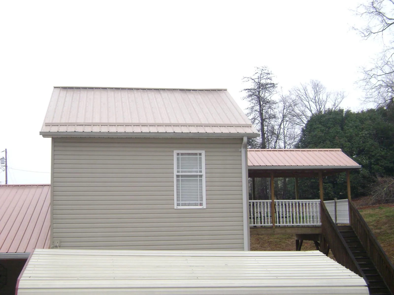 Tan metal roofs on a two story addition and attached porch, from a Roof Replacement job in Coal Valley